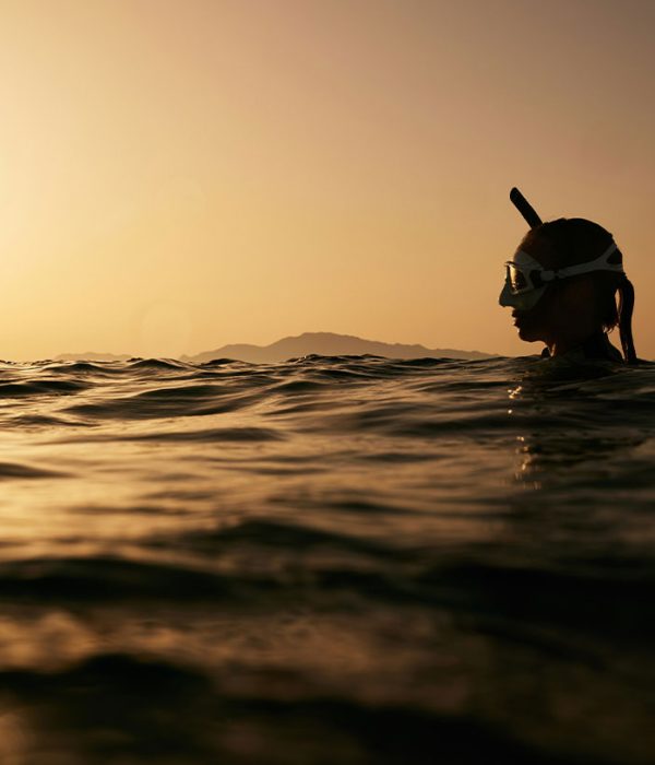 Donna in acqua al tramonto con maschera da snorkeling durante una vacanza tropicale tra mare e relax